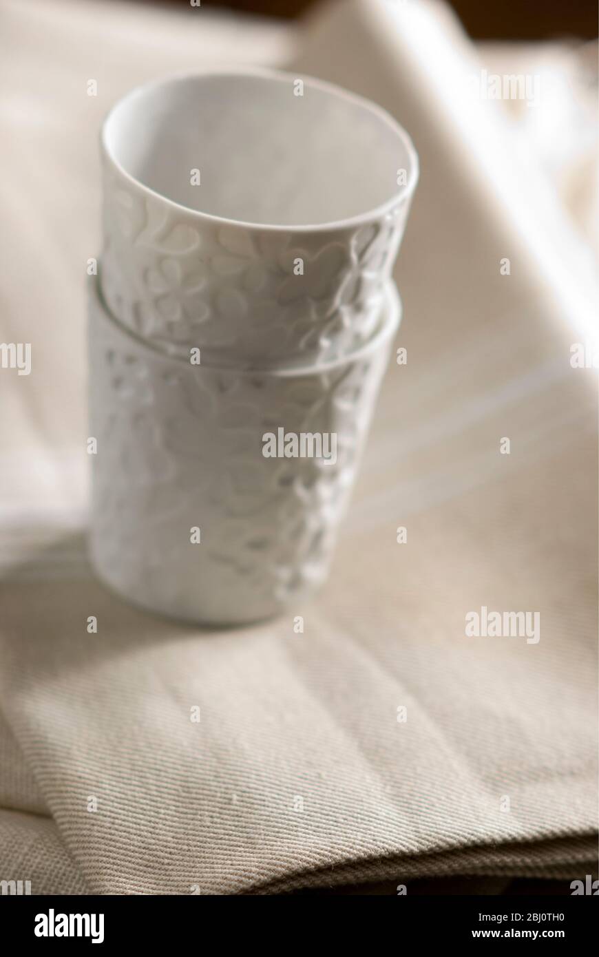 Weiße Porzellanbecher oder Teelicht-Halter auf cremefarbenen Leinentuch gestapelt - Stockfoto