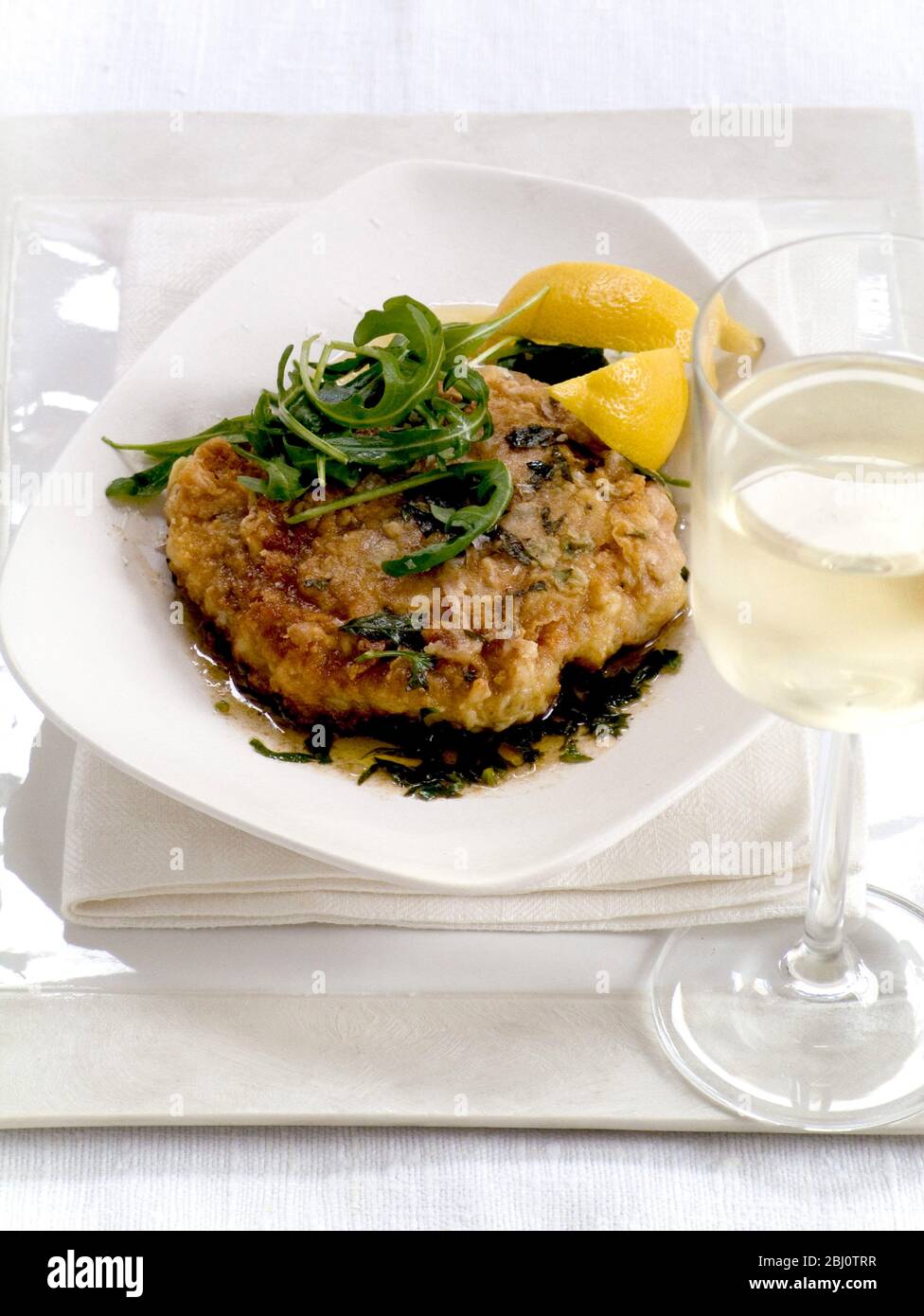 Schweineschnitzel, mit Ei und gewürztem Mehl überzogen, mit Salbei und Zitrone, serviert mit Rucola-Salat, - Stockfoto