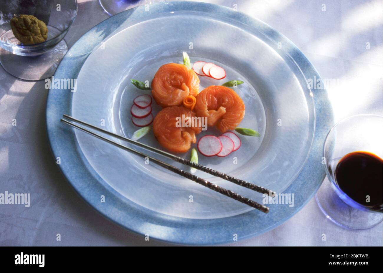 Lachs-Sushi, wunderschön auf einem weißen Milchglas-Teller in formeller Tischumgebung bei der Sommermittagesparty im Freien, mit Wasabi und geriebenen weißen Radis Stockfoto