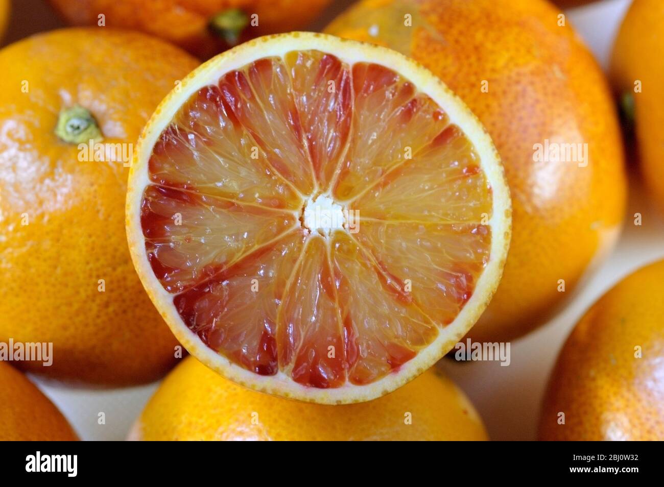 Blutorange, halbiert auf weißer Oberfläche mit ganzen Orangen dahinter - Stockfoto