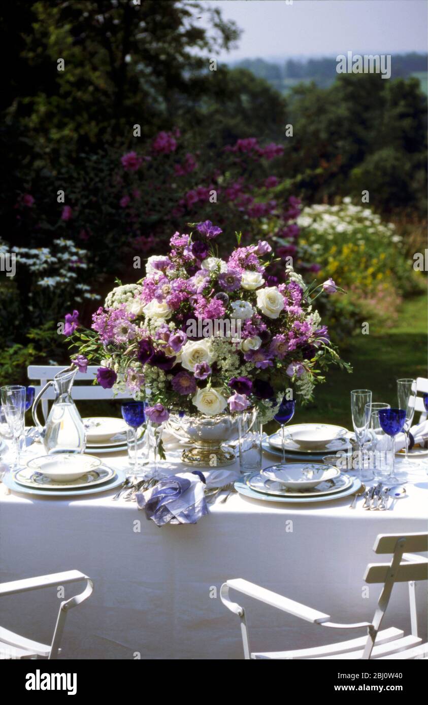 Erstaunliche blau-weiße Blumenarrangement in der Mitte der formalen Tischgestaltung draußen im Sommergarten angeordnet - Stockfoto
