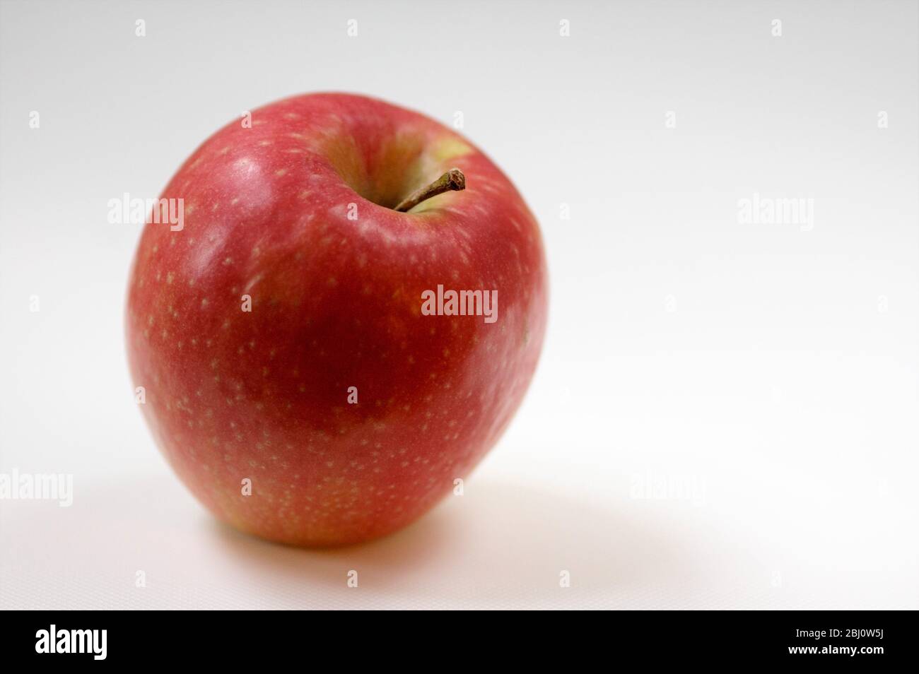 Einzelner glänzender roter Apfel auf weißem Hintergrund - Stockfoto