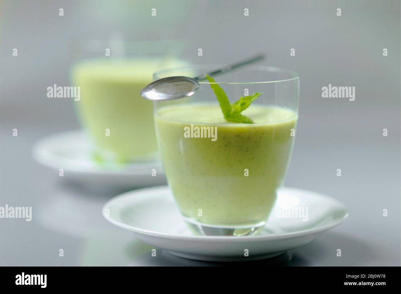 Gekühlte Suppe aus frischen Gartenerbsen und Zucchini in kleinen Gläsern auf weißen Untertassen mit Minzkring garniert - Stockfoto