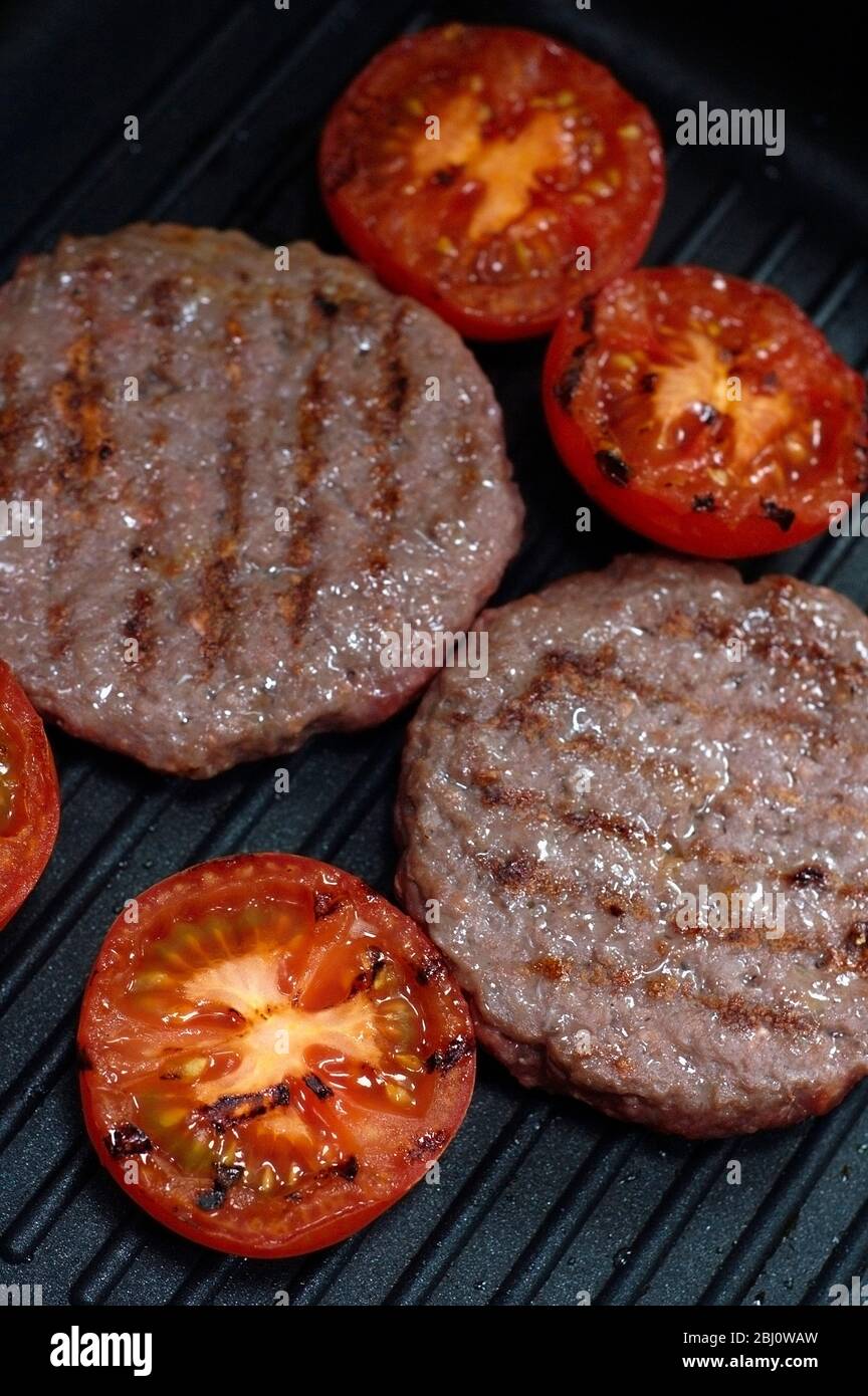 Beefburgers und halbierte Tomaten auf Antihaft-Grillpfanne gegrillt - Stockfoto