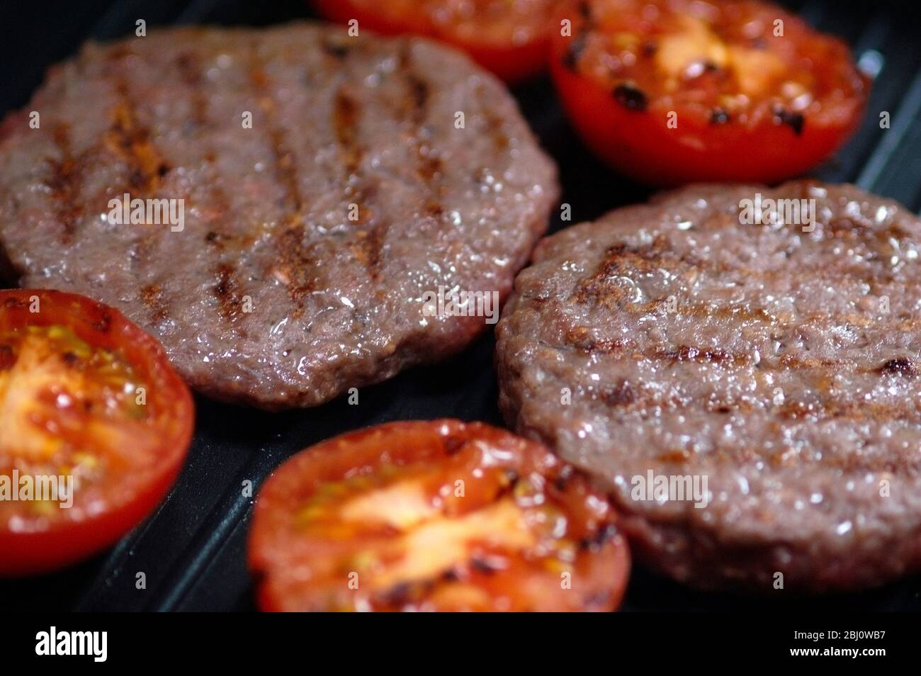 Beefburgers und halbierte Tomaten auf Antihaft-Grillpfanne gegrillt - Stockfoto
