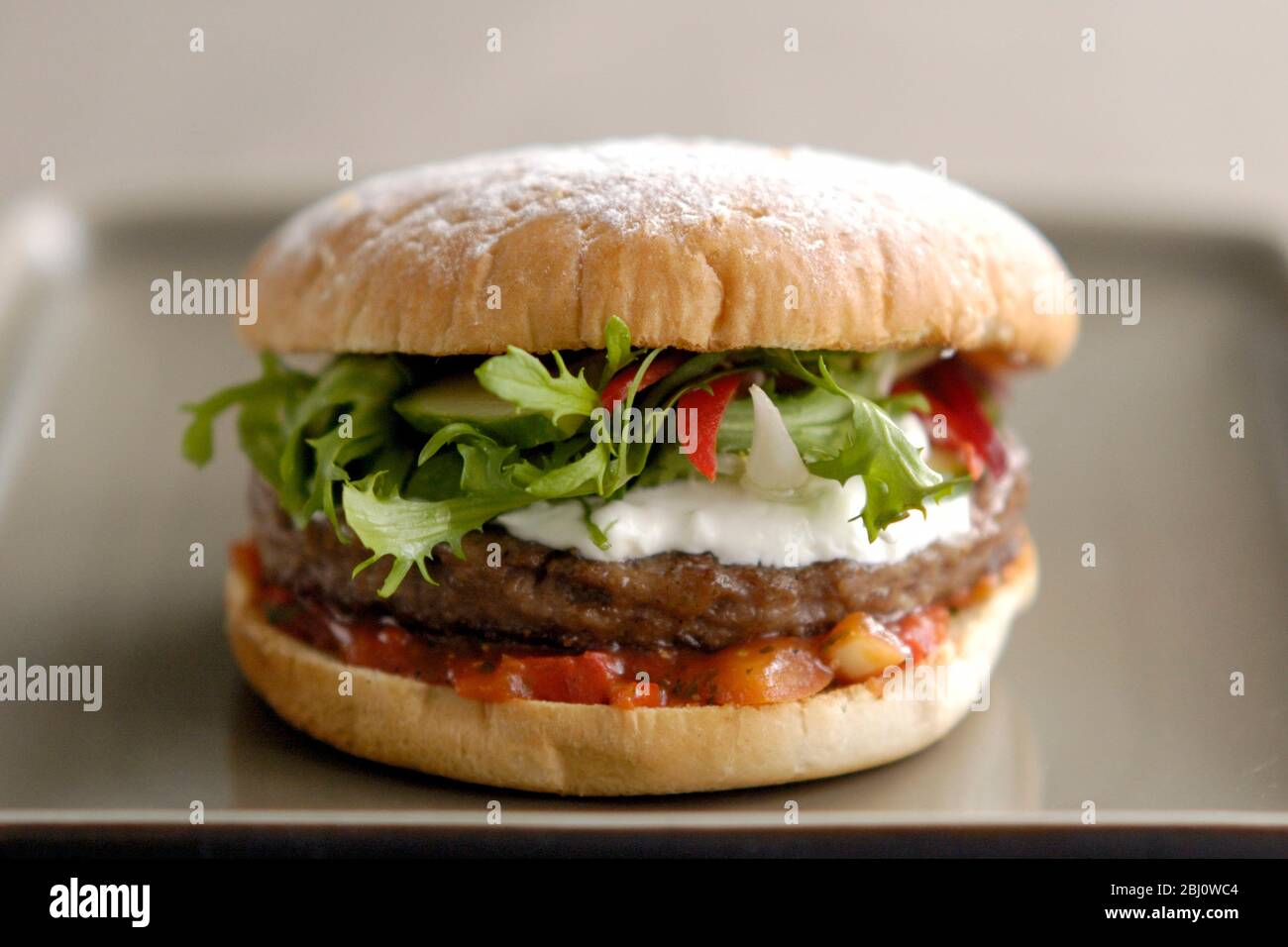 Hamburger vom Grill im Brötchen mit Friseuesalat, Gurke, Pfefferstreifen, Sauerrahm und Tomatensalsa - Stockfoto