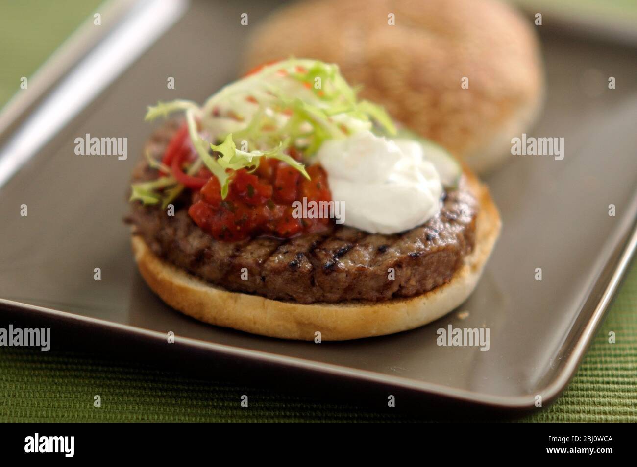 Hamburger vom Grill im Brötchen mit Friseuesalat, Tomatensalsa und saurer Sahne - - Stockfoto
