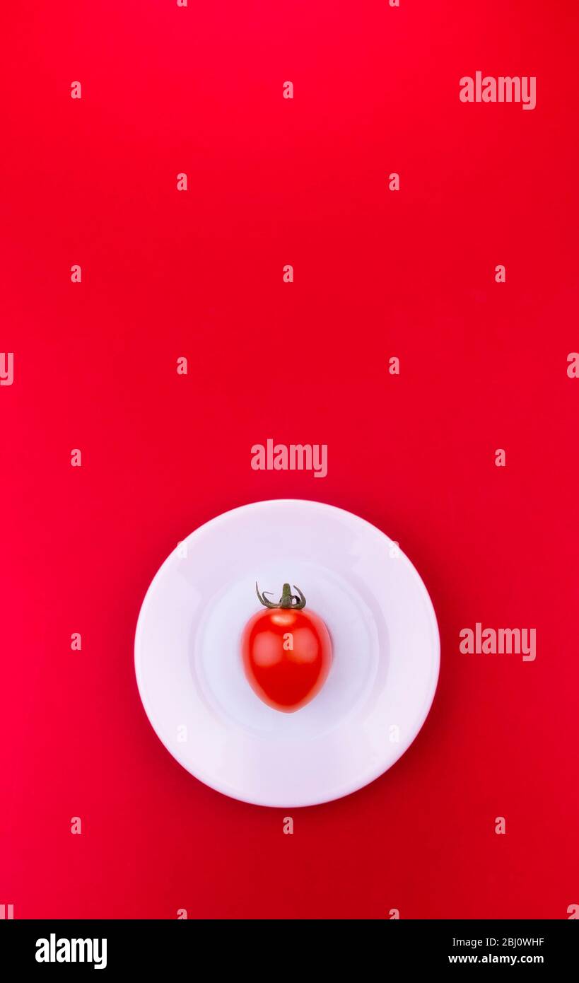 Kirschtomate auf weißem Teller auf rotem Hintergrund platziert Stockfoto