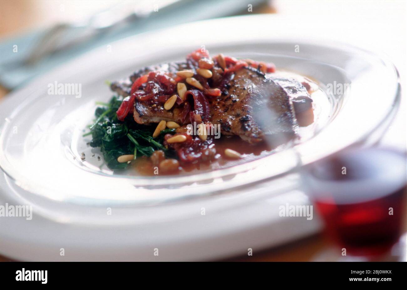 Gebratene Lämmer Leber mit roter Zwiebelsauce, Spinat und gerösteten Pinienkernen auf Glasplatten mit Rotwein - Stockfoto