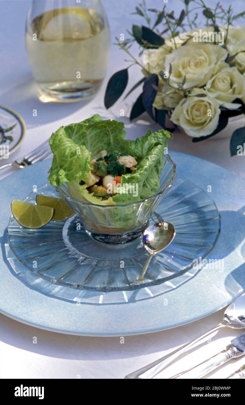 Hummersalat in Salatblättern in Kristallglas-Schüssel in formeller Tischumgebung bei Outdoor Sommer Lunch Party, mit Rosen und Weißwein - Stockfoto