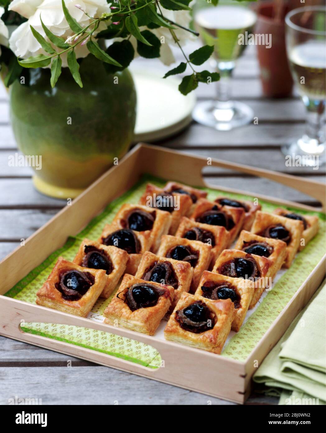 Canapes mit Oliven in Sardellen auf kleinen Plätzen Blätterteig gebacken gewickelt auf Gartentisch im Freien serviert - Stockfoto