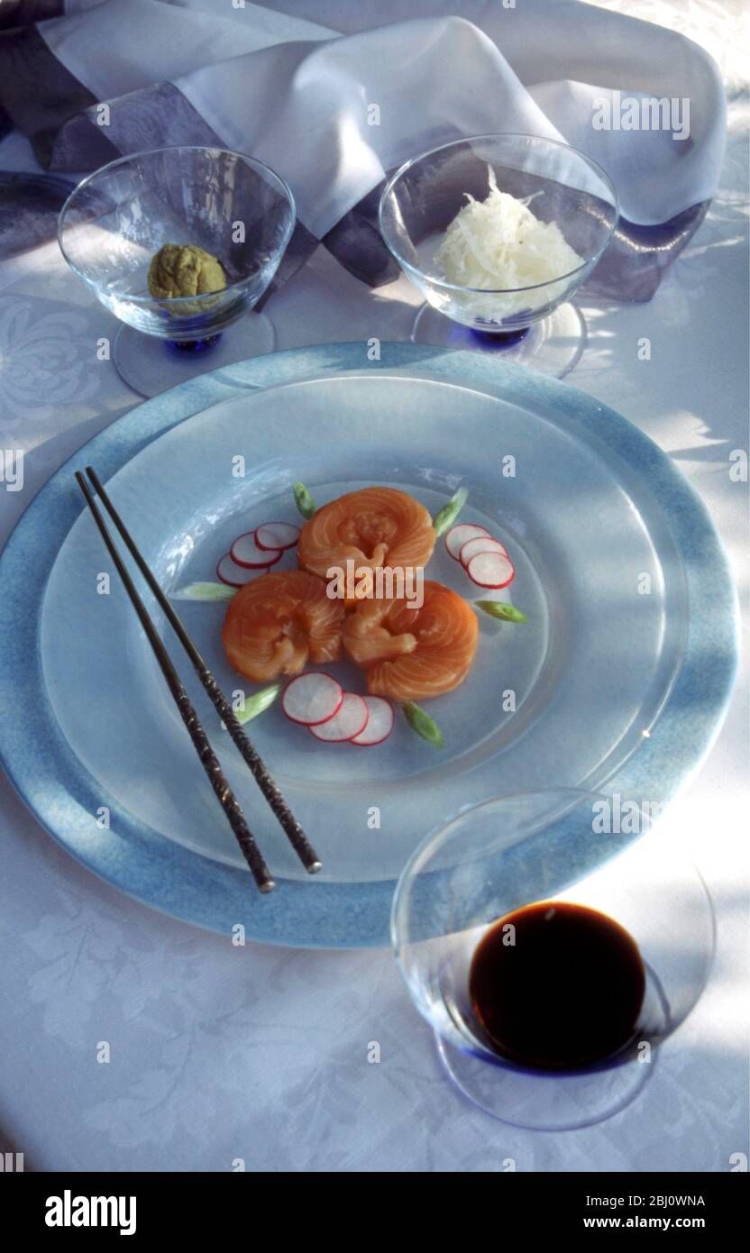 Lachs-Sushi, wunderschön auf einem weißen Milchglas-Teller in formeller Tischumgebung bei der Sommermittagesparty im Freien, mit Wasabi und geriebenen weißen Radis Stockfoto
