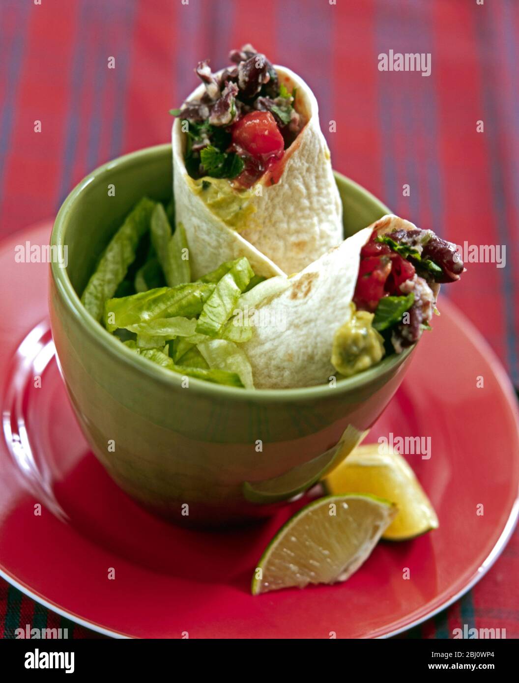 Leichtes Mittagessen mit Chili-Bohnen-Mischung in weichen Tortillas mit Salat und Zitronenstücke in grüner Schüssel verpackt - Stockfoto