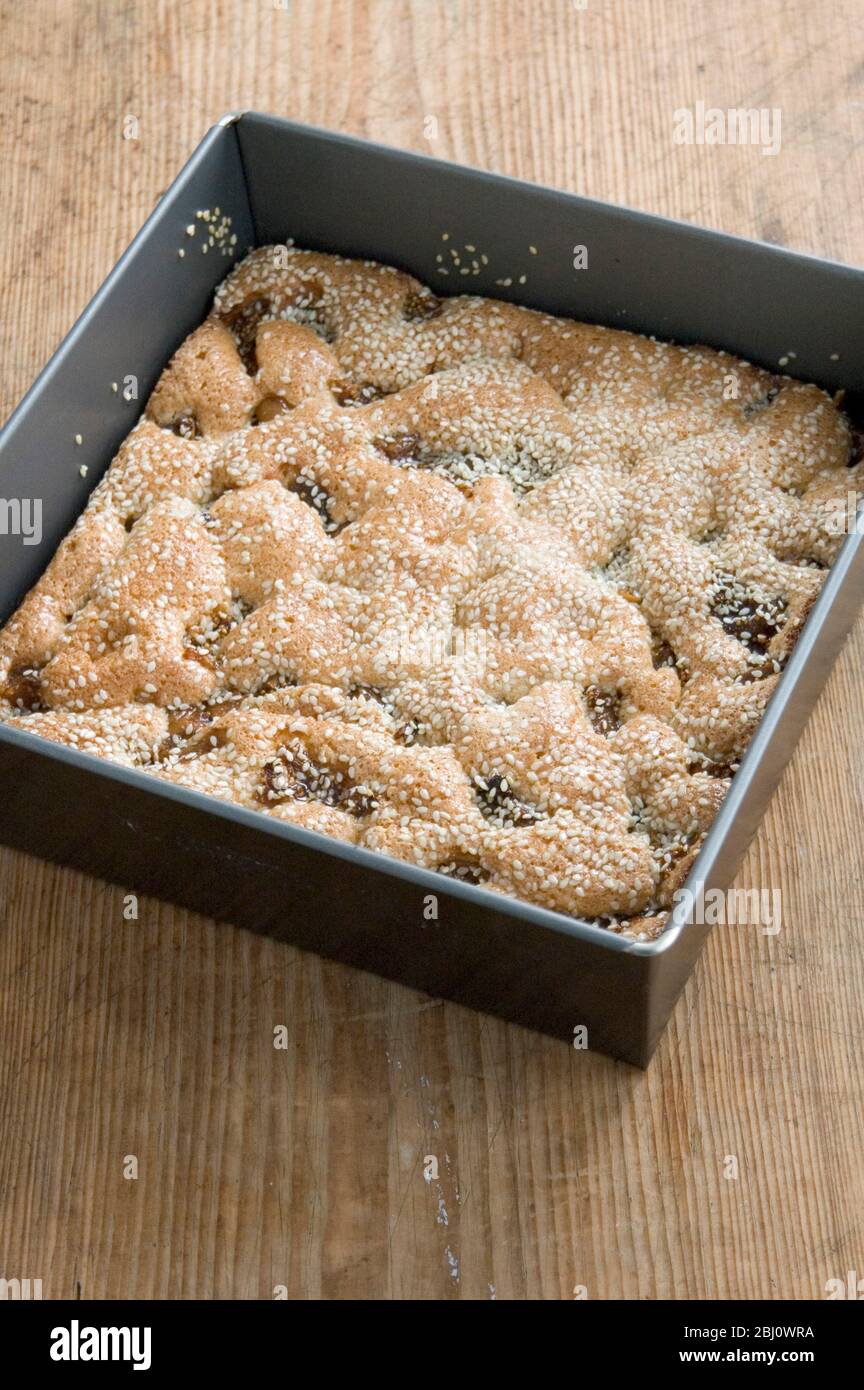 Grießkuchen mit Feigen und Sesam noch in seinem quadratischen Tablett auf dem Küchentisch - Stockfoto