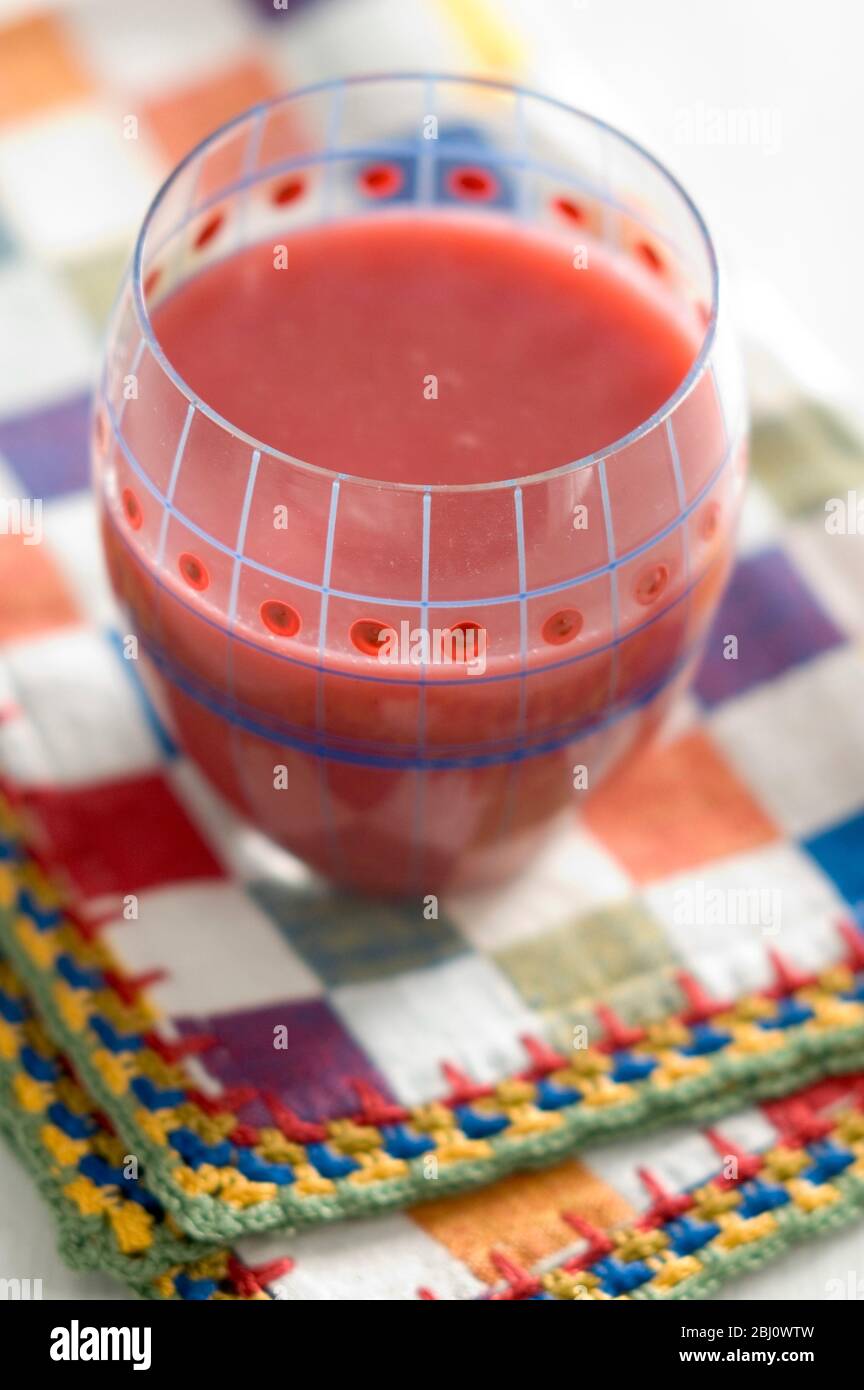 Dekorativ bemaltes Glas von rotem Himbeer-Smoothie auf hell karierter Serviette - Stockfoto