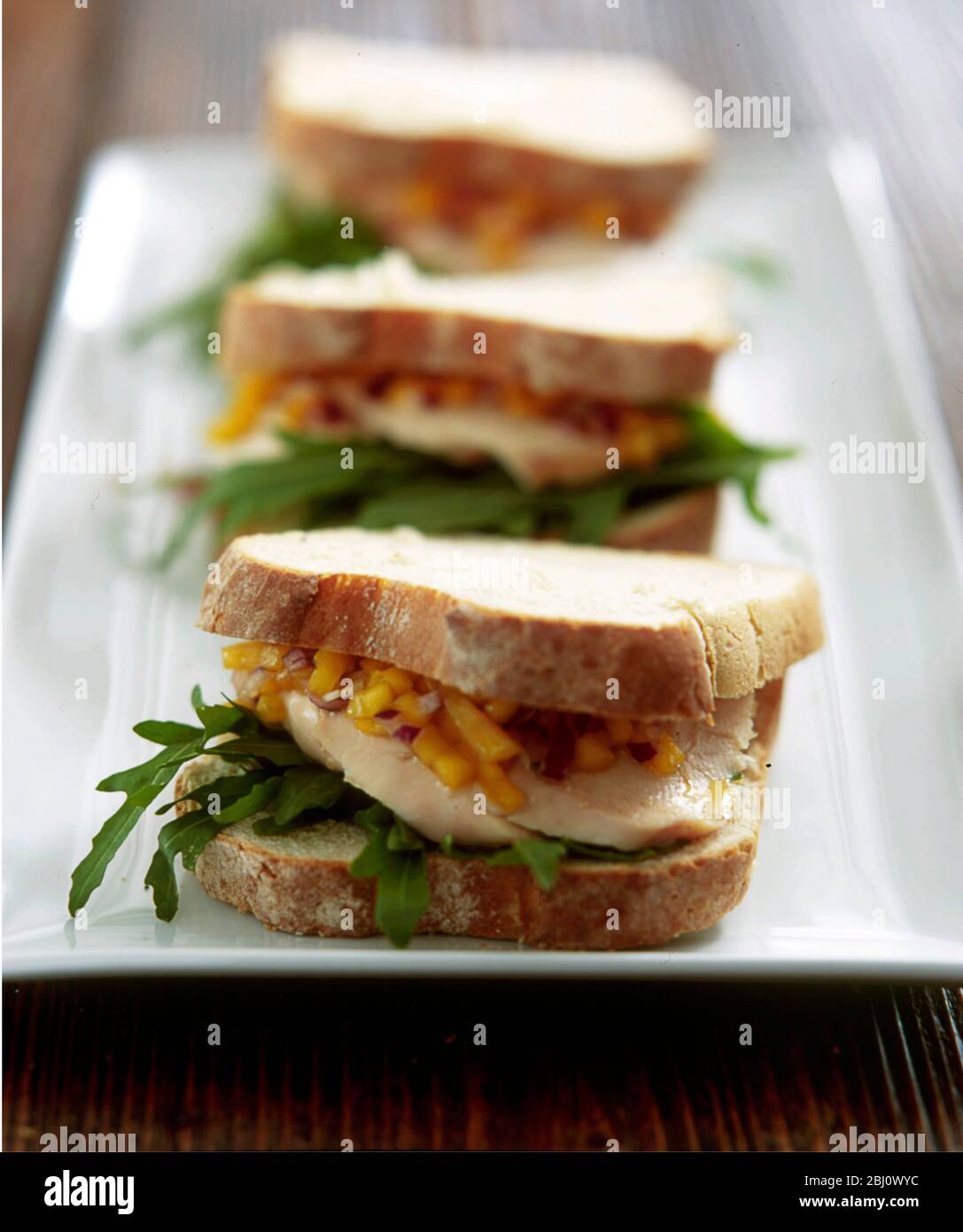 Reihe von drei weißen knusprigen Brot Sandwiches mit Huhn, Rucola und Mango genießen auf langen weißen Teller - Stockfoto