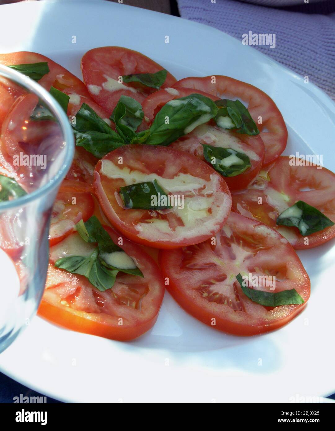 Tomatensalat mit Dressing und frischem Basilikum im französischen Freiluftrestaurant am Meer in Menton, Südfrankreich - Stockfoto