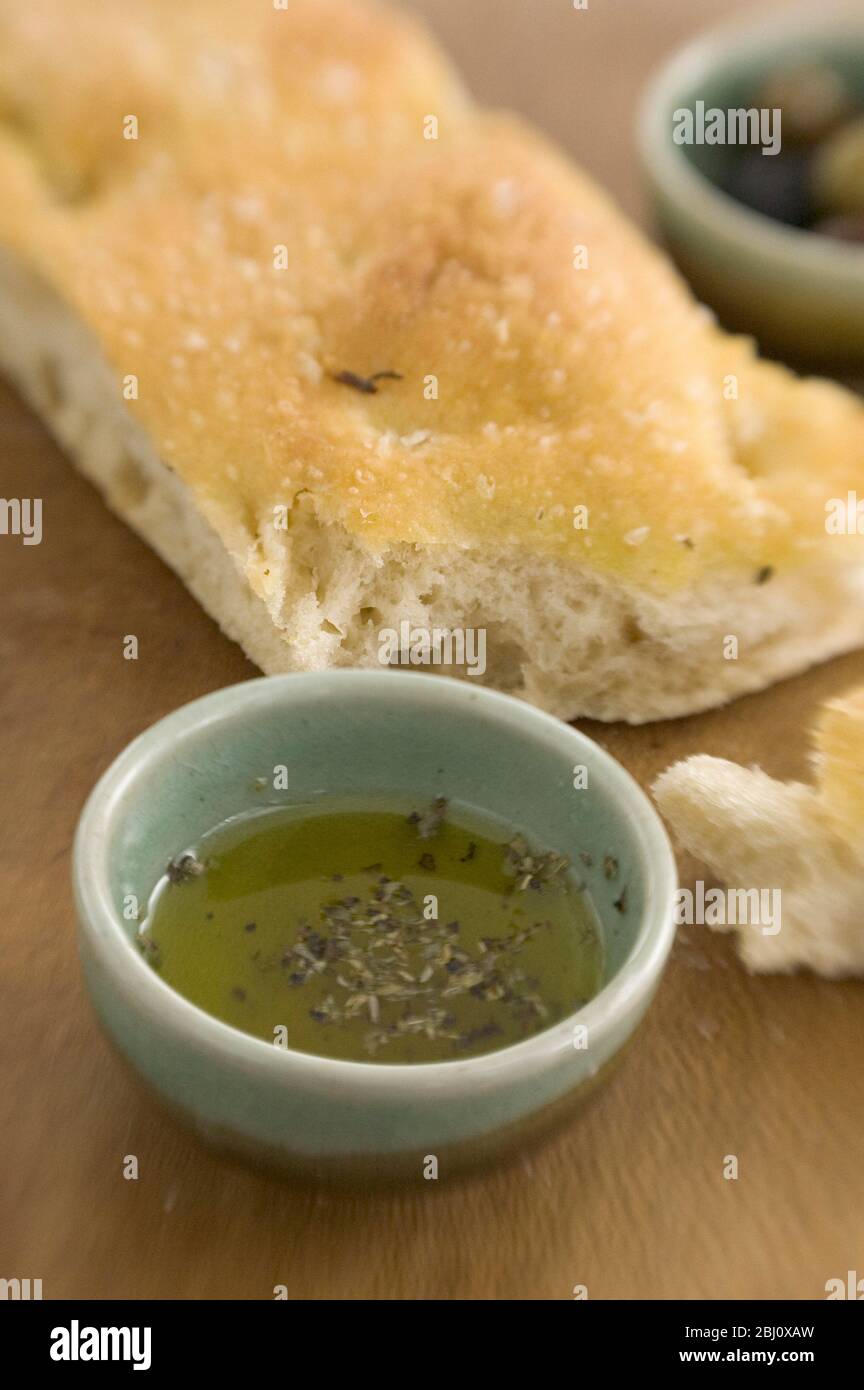 Olivenöl und Rosmarin Foccaccia Brot auf Holzbrett mit kleinen Schüsseln von einkerkerntem Olivenöl und ganze Oliven. Aufgenommen mit Objektiv für Lenskimitoren - Stockfoto