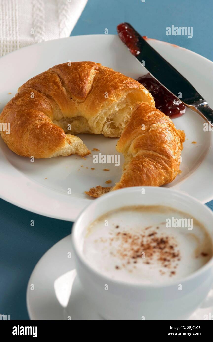 Croissant mit einer Tasse Cappuccino auf weißem Geschirr - Stockfoto