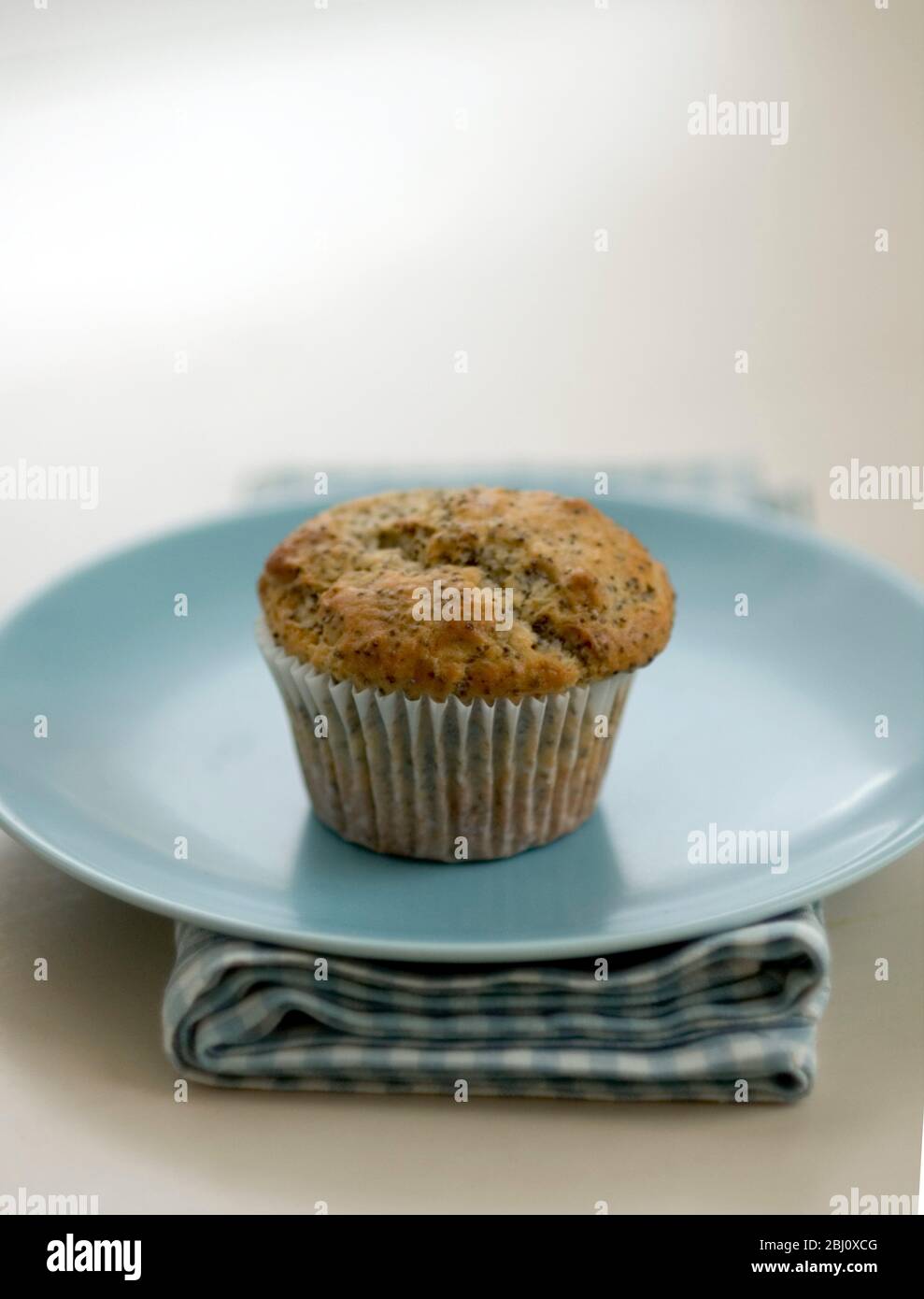 Single Moppyseed Muffin auf blauer Platte auf Karo Serviette, auf bemalten Tisch. - Stockfoto