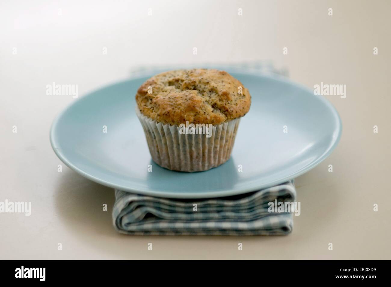 Single Moppyseed Muffin auf blauer Platte auf Karo Serviette, auf bemalten Tisch. - Stockfoto