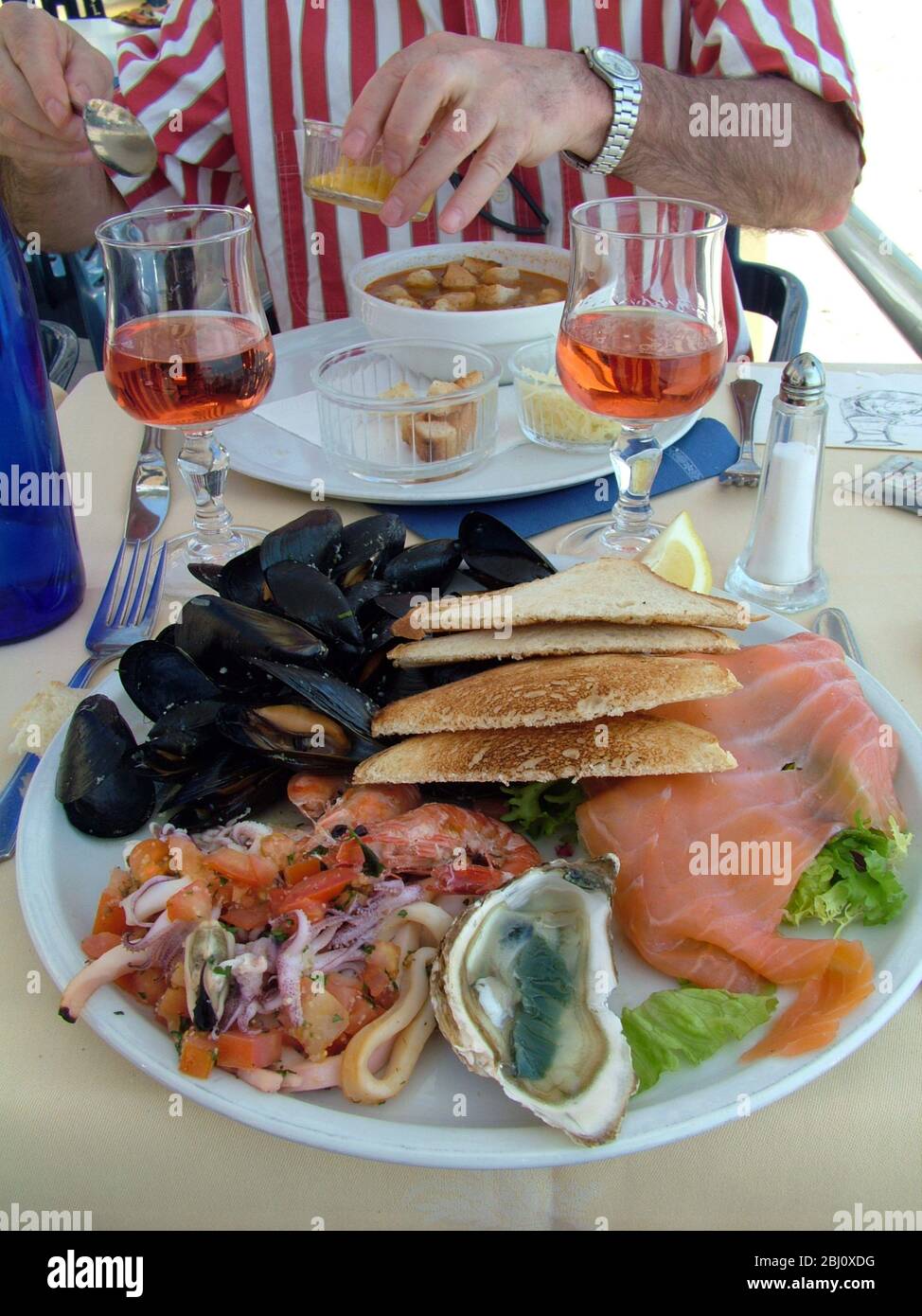 Riesige gemischte Meeresfrüchte Platte auf dem Tisch des Restaurants am Meer in Menton, mit Abendessen gegenüber mit klassischen französischen Fischsuppe mit Croutons und Rouille - Stockfoto