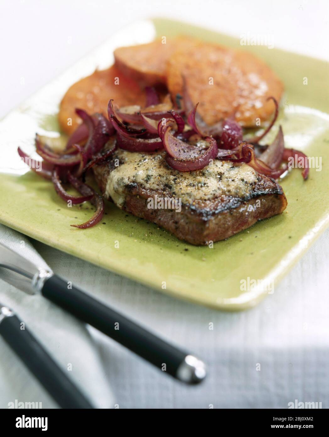 Dickes Schweinekotelett serviert mit Käse, roten Zwiebeln und Süßkartoffel auf grünem Teller - Stockfoto