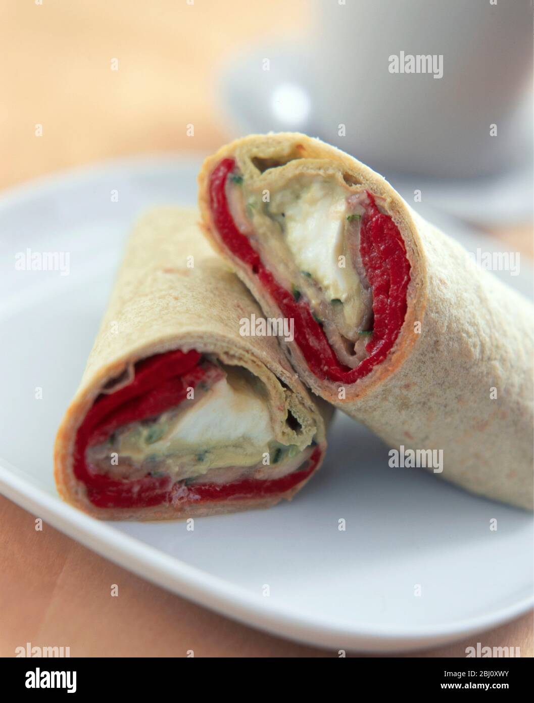 Wrap Sandwich in zwei geschnitten auf weißem Teller mit Tasse und Untertasse dahinter angeordnet - Stockfoto