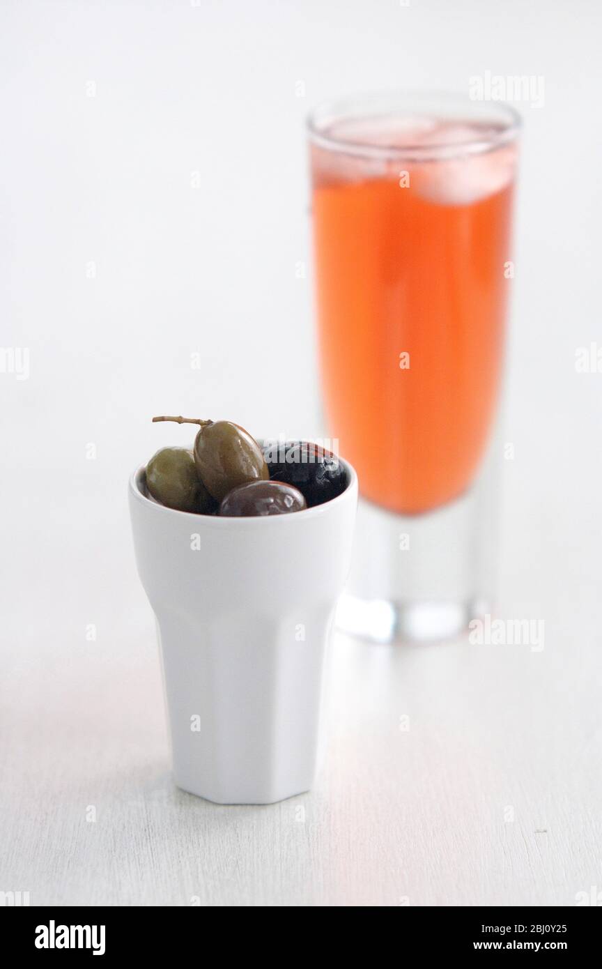 Ein Glas Campari und kleine weiße Keramiktopf mit italienischen Oliven - Stockfoto