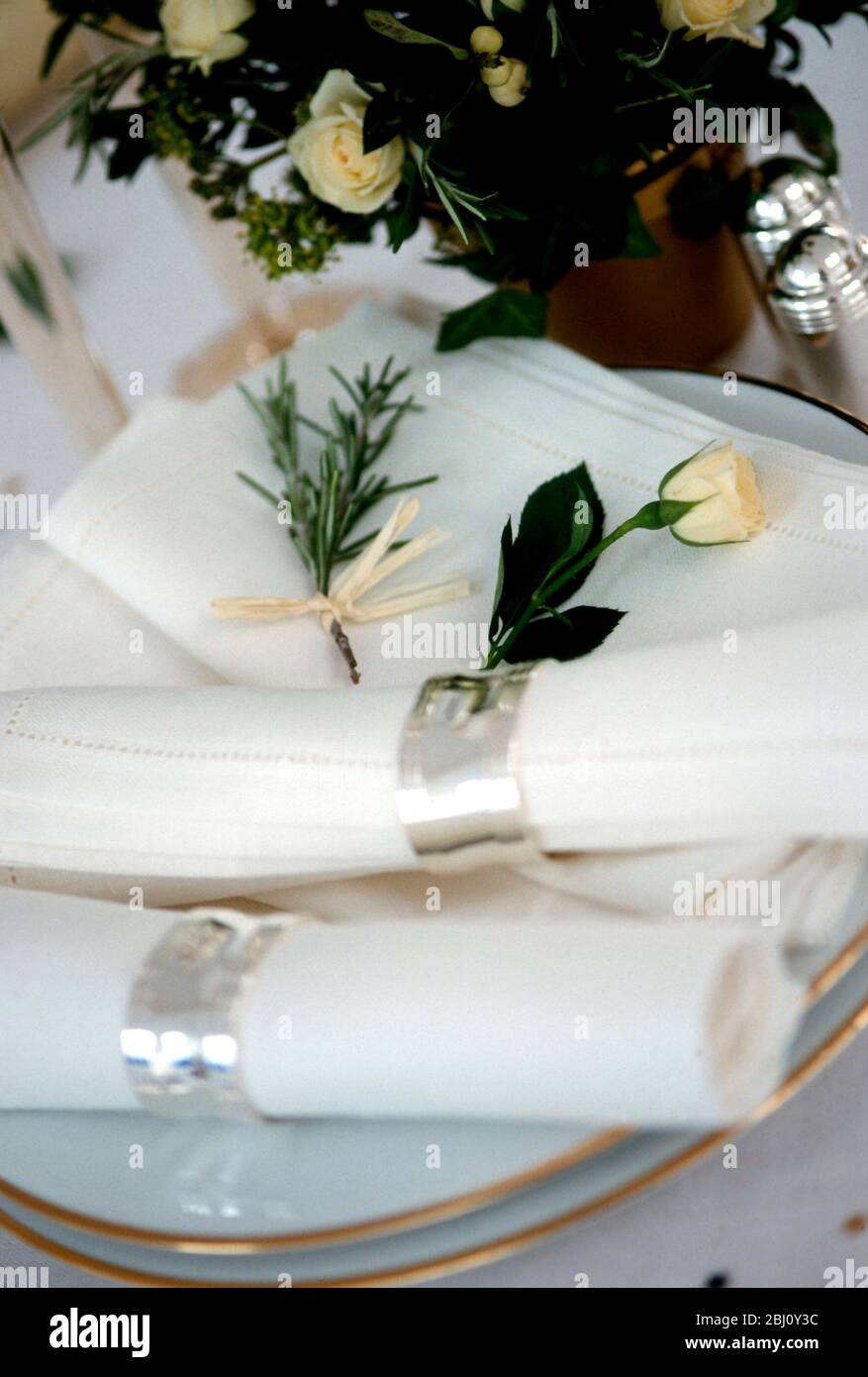 Servietten in silbernen Ringen mit Rosenknospen und goldgerandeten Tellern, bereit zum Auslegen für Hochzeitstisch - Stockfoto