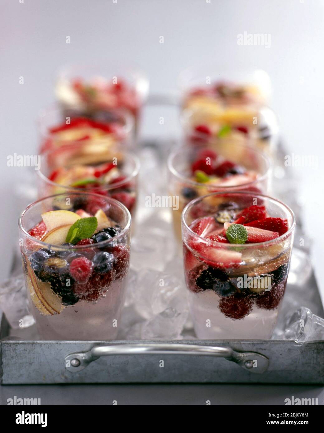 Acht Gläser frisches Obst und Mineralwasser auf Metall, eisküchelgefülltes Tablett - Stockfoto