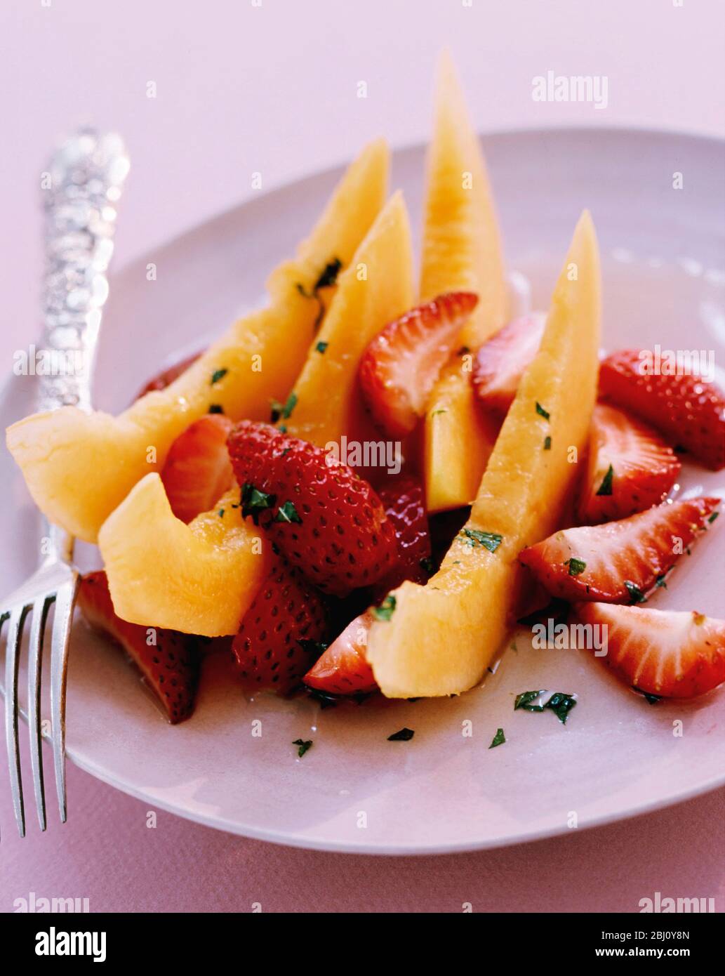 Dessertplatte mit frischem Obstsalat aus geschnittenen Erdbeeren und Melonenpfeilchen - Stockfoto