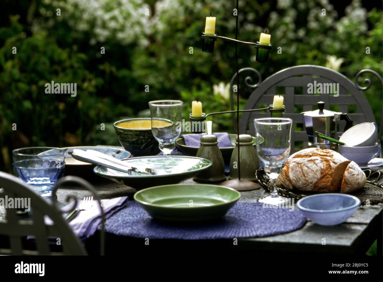 Grüne und blaue Keramik und Glas auf Gartentisch gelegt für Abendessen im Freien - Stockfoto