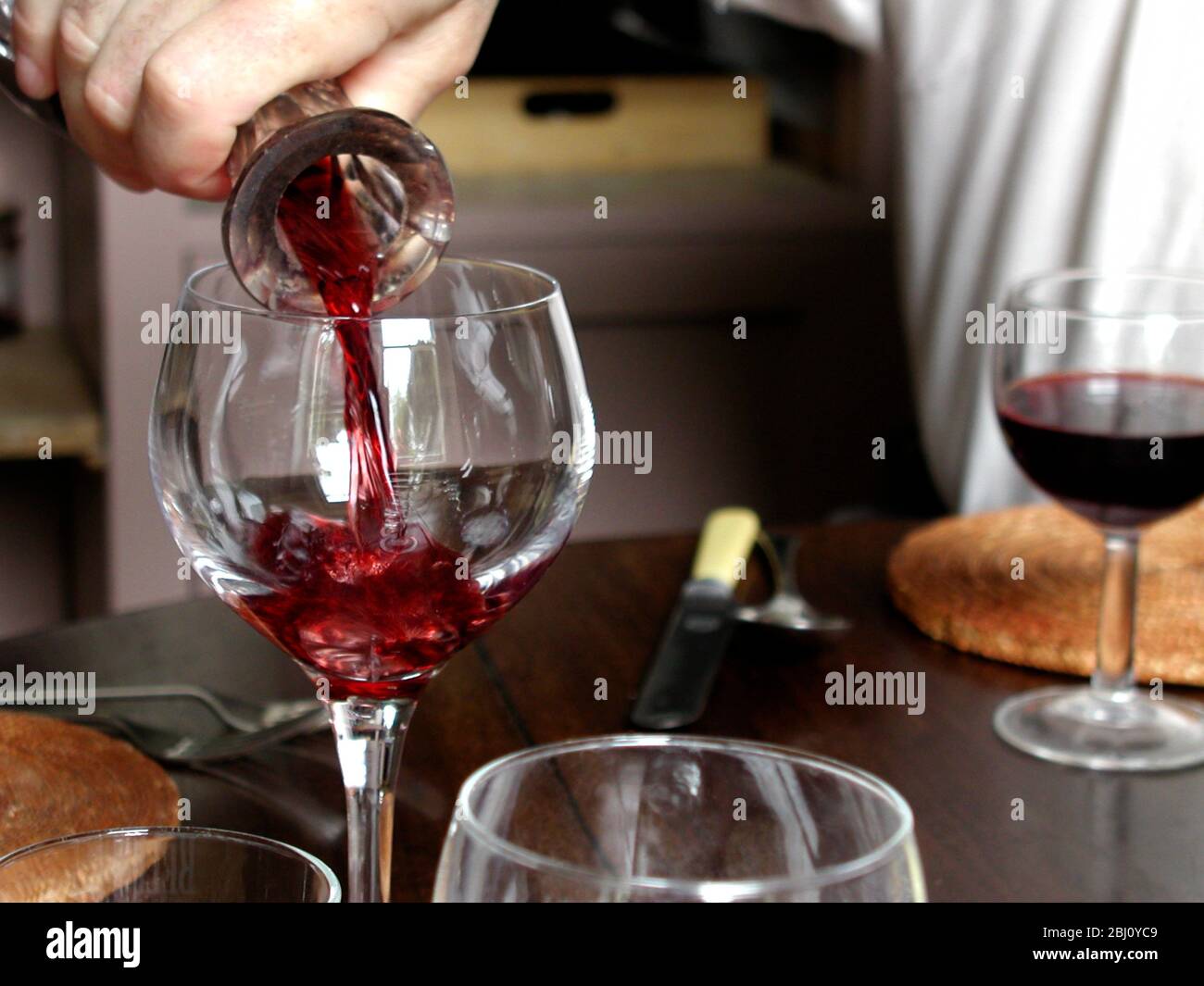 Rotwein wird aus Kristalldekanter in großes klassisches Weinglas am Esstisch gegossen - Stockfoto