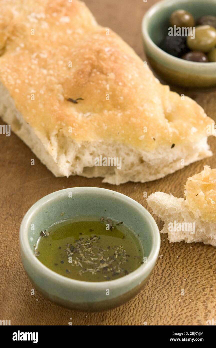 Olivenöl und Rosmarin Foccaccia Brot auf Holzbrett mit kleinen Schüsseln von einkerkerntem Olivenöl und ganze Oliven - Stockfoto