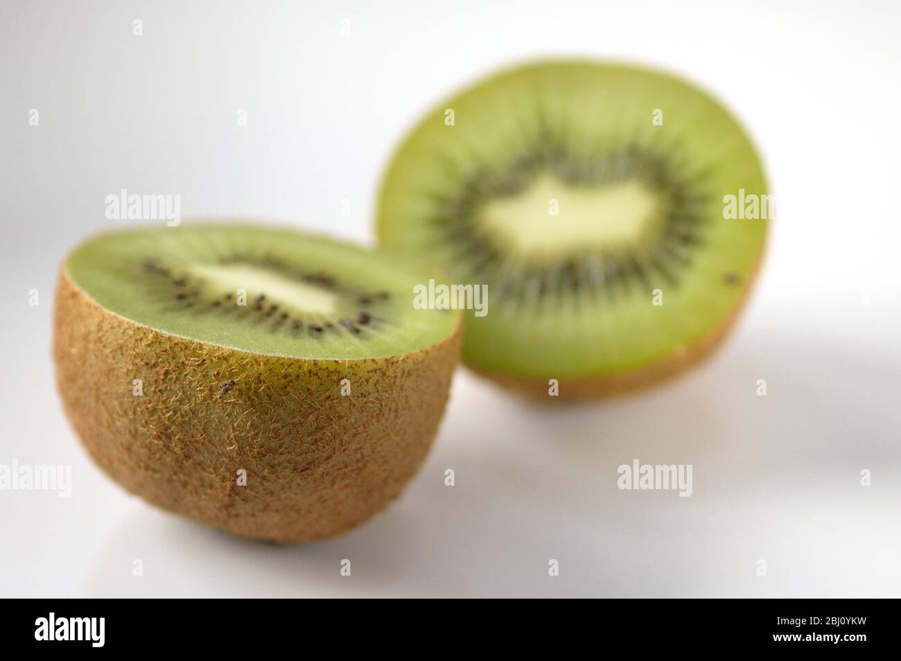 Kiwi-Frucht halbiert, um innere Textur und Struktur auf weißer Keramik-Oberfläche zu zeigen - Stockfoto