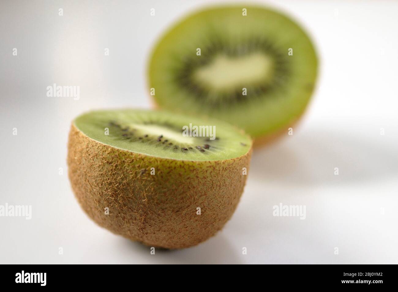 Kiwi-Frucht halbiert, um innere Textur und Struktur auf weißer Keramik-Oberfläche zu zeigen - Stockfoto