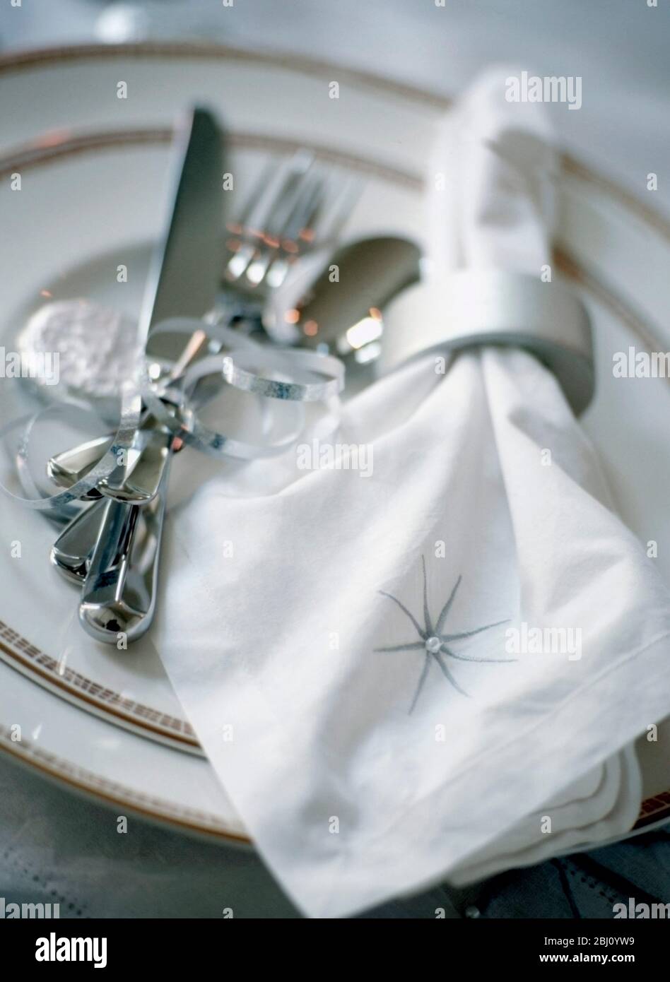 Festliche Tischkulisse in Weiß und Silber mit bestickter Serviette, Bändern und Süßigkeiten - Stockfoto