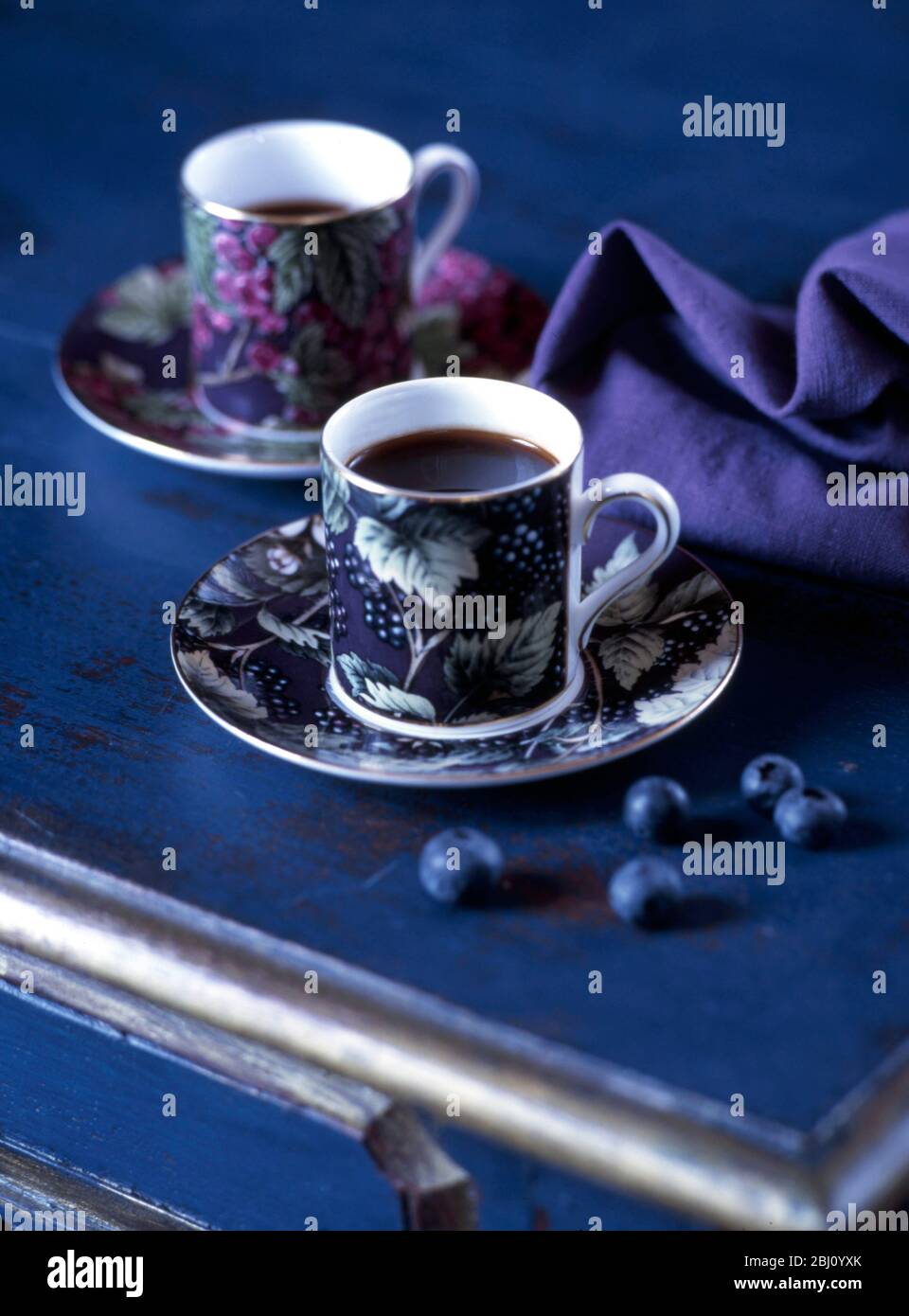 Ein Paar dekorierte Kaffeetassen auf dunkelblauer Oberfläche mit Serviette und Blaubeeren - Stockfoto