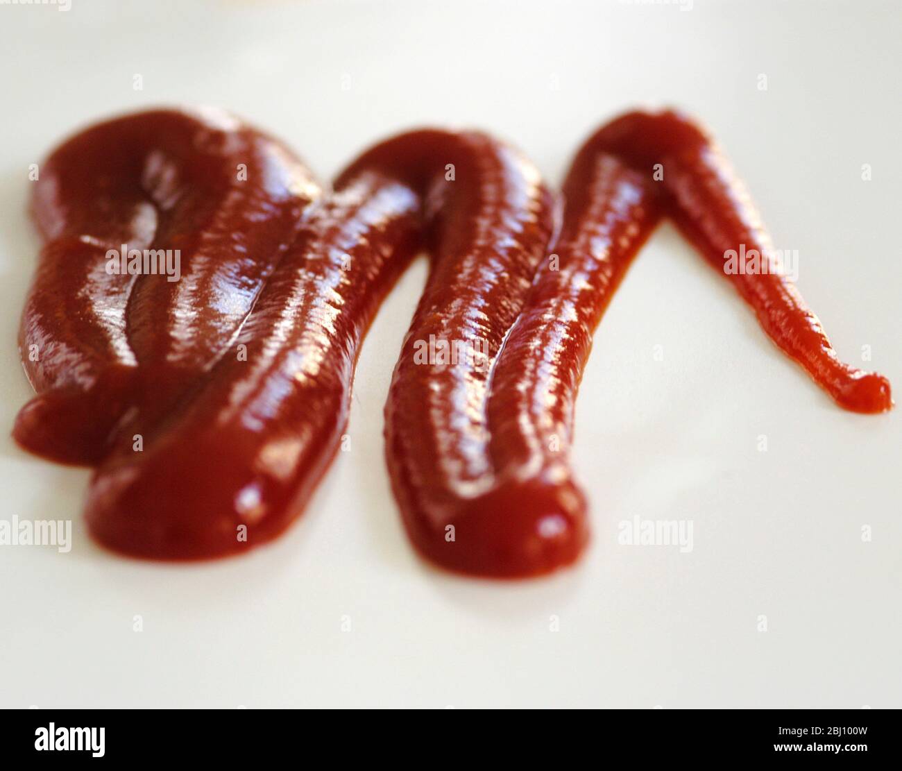 Squiggle von Tomatenketchup aus der Flasche gepresst auf weißem Hintergrund. Kurze Schärfentiefe. - Stockfoto
