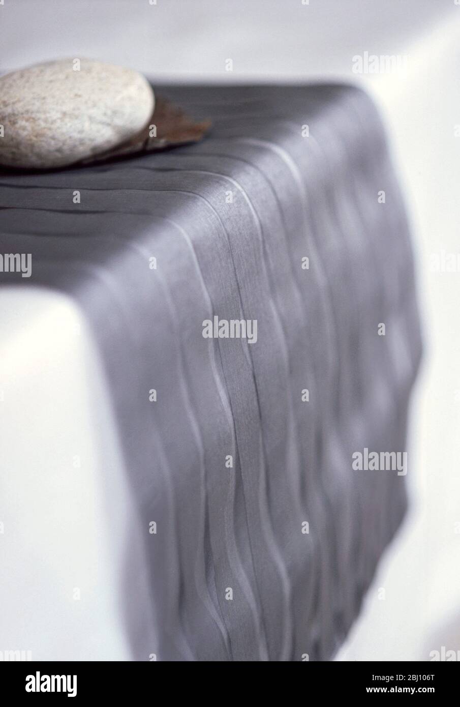 Gefaltetes graues Seiden-Organza als Tischläufer mit großem Kieselstein als Dekoration - Stockfoto