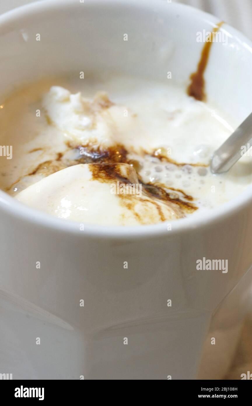 Eistkaffee mit Vanilleeis und Schokoladensirup in weißem Becher auf kariertem Liinen-Tuch - Stockfoto