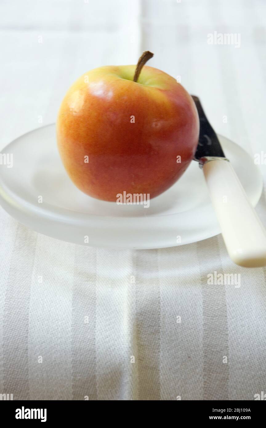 Ein Apfel auf einer geschliffenen Glasplatte mit Messer - Stockfoto