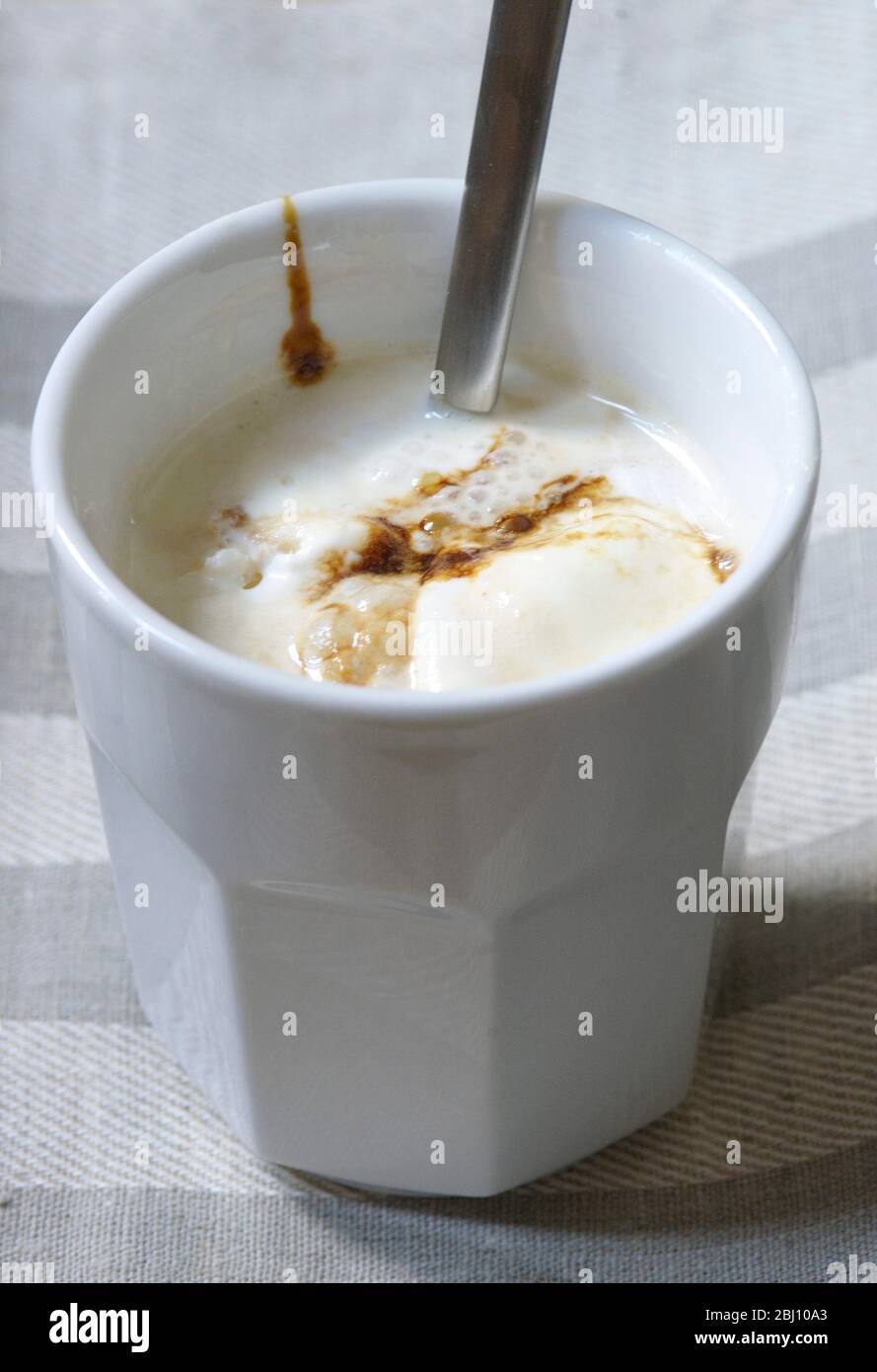 Eistkaffee mit Vanilleeis und Schokoladensirup in weißem Becher auf kariertem Liinen-Tuch - Stockfoto