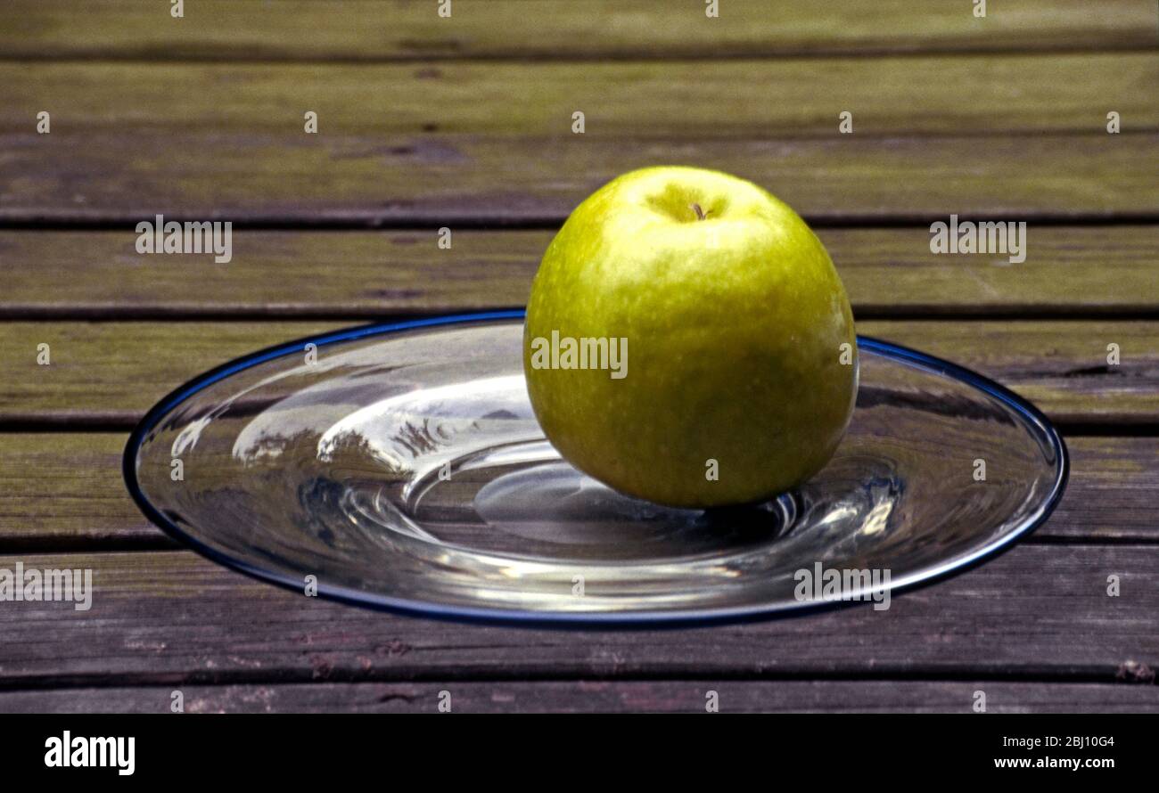 Grüner Apfel auf Klarglas-Platte auf altem Holztisch - Stockfoto