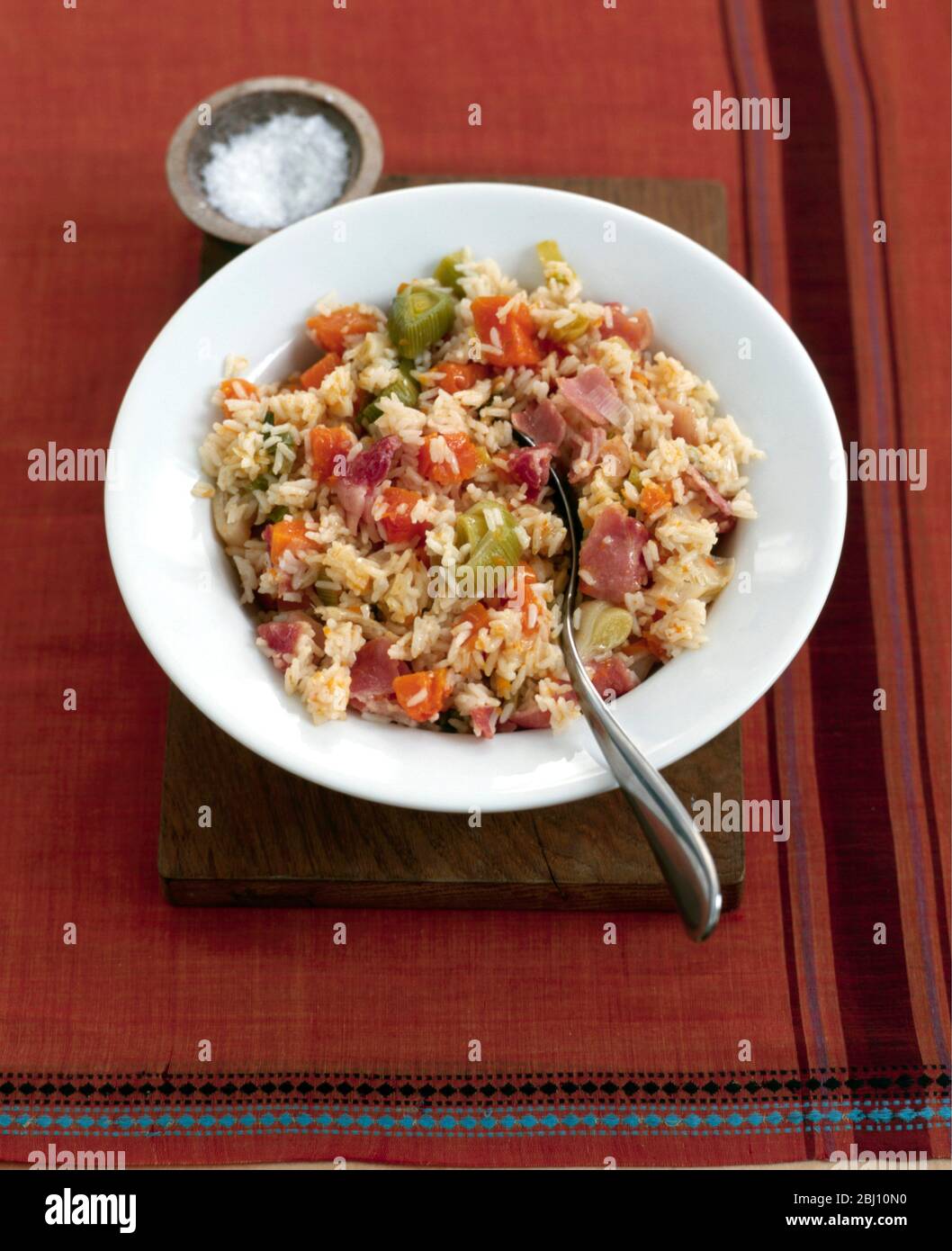 Teller mit Gemüse-Risotto auf tiefem weißen Teller auf Holzbrett mit kleiner Salzschale - Stockfoto