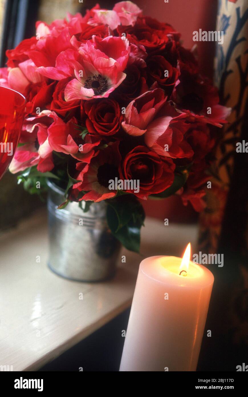 Strauß roter Rosen und Anemonen in Metallblumeneimer mit Kerze - Stockfoto