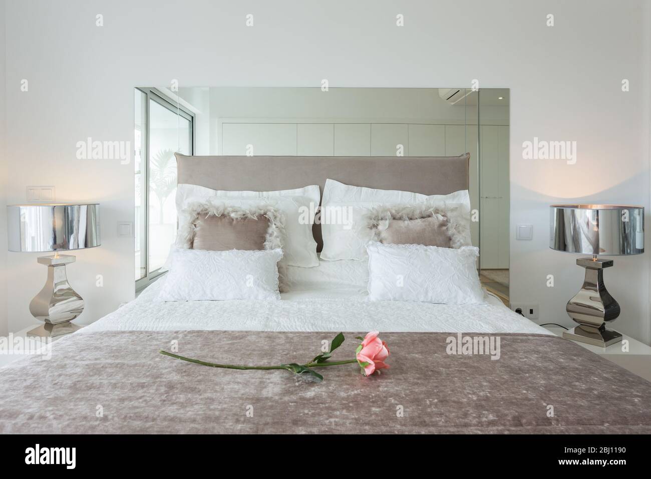 Schlafzimmer mit moderner Dekoration für eine komfortable und romantische Nacht. Großes Bett mit wunderschöner Bettwäsche und eine Rose für den Valentinstag. Stockfoto