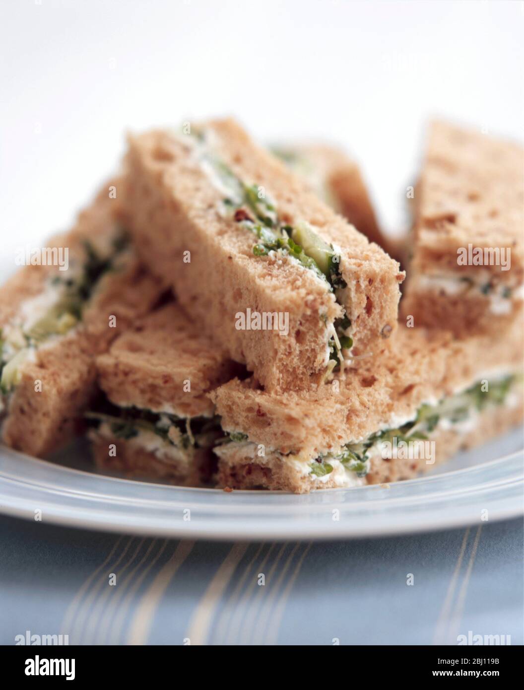 Kleine Sandwiches aus braunem Brot, in Finger geschnitten mit Frischkäse, Gurke, Kresse und getrockneten Tomaten - Stockfoto