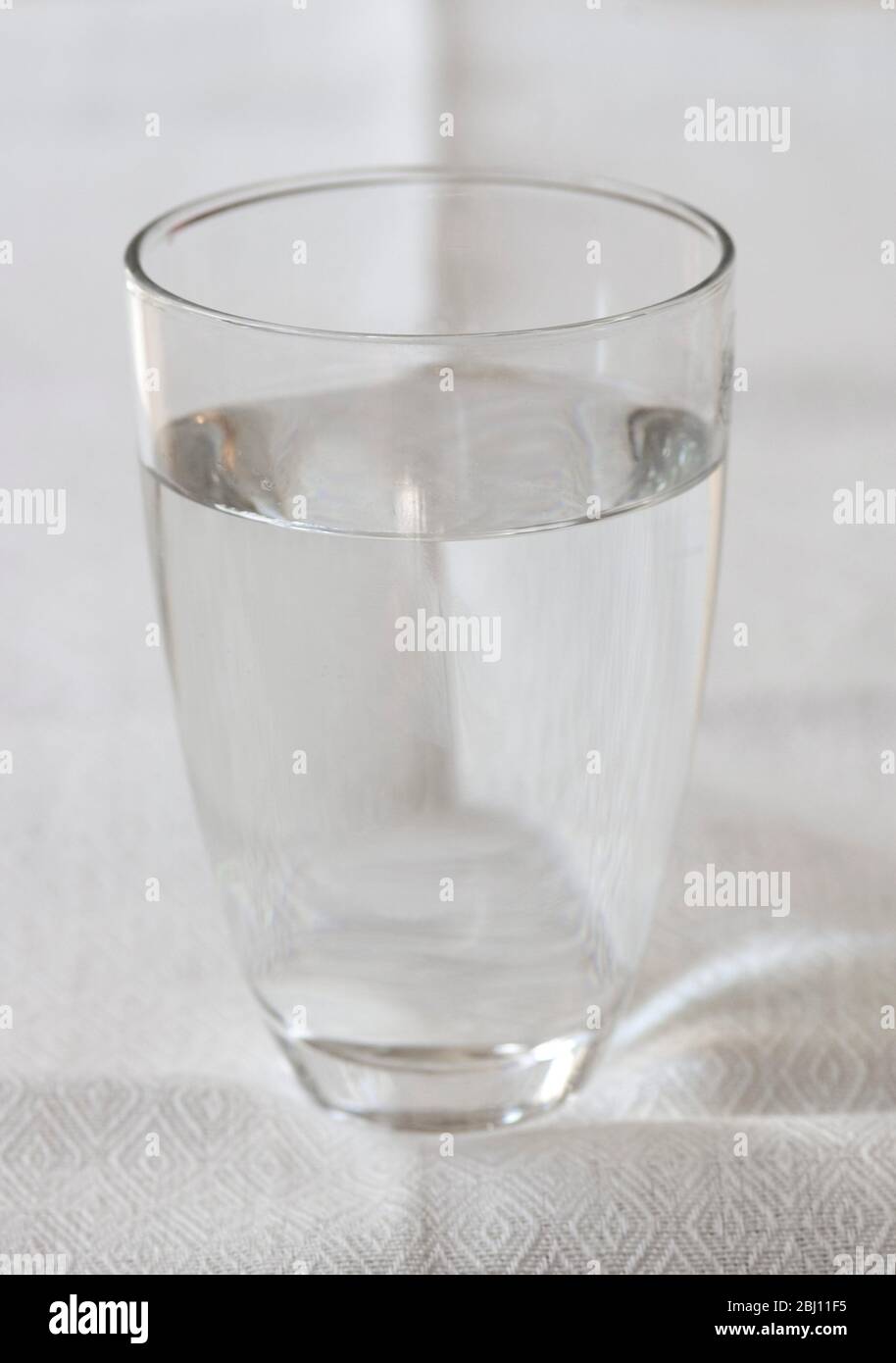 Einfaches handgeblasenes Glas mit klarem Wasser auf cremefarbenem Leinentuch - Stockfoto
